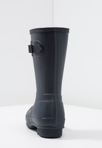 Botte de pluie en caoutchouc noir avec un bout rond, une surface texturée et un détail de boucle sur le côté. Bord supérieur légèrement cintré et semelle plate.