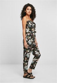 Lillelilleline kombinesoon mustast kangast, millel on rihmata ülaosa, elastne vöökoht ja kitsenevad jalad, mis on kaunistatud värvikate troopiliste mustritega. Mustad sisejalatsid.