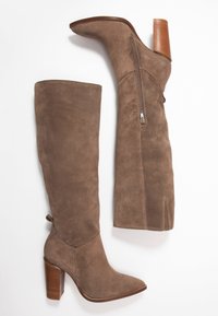 Botas de ante marrón que cubren hasta encima de la rodilla, con punta afilada, tacón cuadrado redondeado y cremallera lateral. El tacón texturizado tiene ranuras verticales.