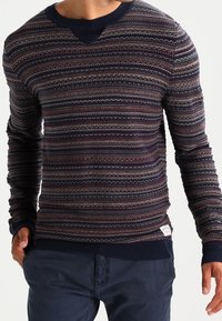 Marinblå tröja med flerfärgade, mönstrade ränder. Ribbat halsringning och ärmslut. Har en liten logotagg i nedre vänstra hörnet. Slimmad design.