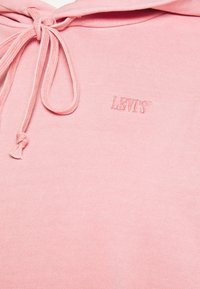 Vaaleanpunainen ribbineuloksesta valmistettu huppari, jossa on kiristysnaru ja kirjailtu "LEVI'S"-logo. Sileä pinta ilman kuvioita tai korostuksia.