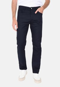 Pantaloni slim-fit blu navy realizzati in cotone, dotati di una tasca frontale e chiusura con un solo bottone. Abbinati a sneakers bianche.