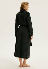 Czarna, długosleeve szata uszyta z miękkiego materiału, posiada szalowy kołnierz, pasek w talii oraz subtelne detale w przeszyciach wzdłuż mankietów.