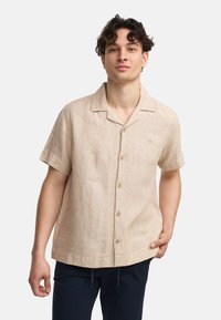 Camisa de lino en color beige claro de manga corta con cuello, presenta un cierre frontal de botones y una textura sutil. Sin patrones ni acentos metálicos notables.