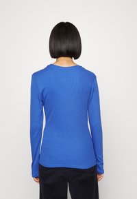 Modrý top s dlouhým rukávem, žebrovaná textura, kulatý výstřih, přiléhavý střih. Hladká látka, jednoduchý styl bez ozdob.
