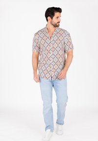Camisa de manga corta con un patrón ondulado multicolor en naranja, azul y crema; combinada con jeans azul claro y zapatillas blancas.