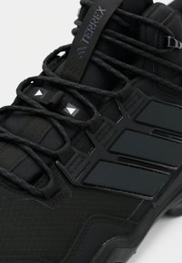 Close-up van een zwarte Adidas Terrex wandelschoen met gestructureerde stof, veters en drie donkere strepen aan de zijkant.