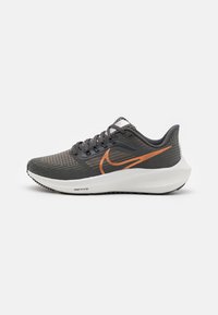 Zapatillas deportivas grises con parte superior texturada, logo de swoosh naranja, entre suela blanca y suela de goma negra. Incluye cordones y un patrón sutil.