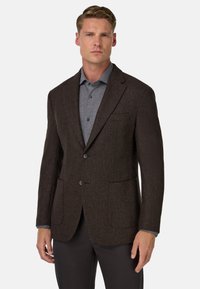 Brązowa blazer z fakturowanej tkaniny, z klapami, dwoma przednimi kieszeniami i zapięciem na jeden guzik, nałożona na szary koszulę.