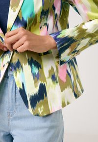 Colorful, patterned blazer with a fitted design. Features a mix of green, pink, and blue hues. Smooth fabric with a structured collar and buttons.