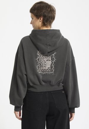 Grijze cropped hoodie met een groot, uitgebreid grafisch ontwerp op de achterkant. Heeft een capuchon en een strak gebreide tailleband. Gemaakt van zachte stof.