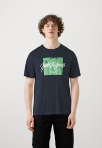 T-shirt in cotone blu navy con stampa grafica verde e bianca con il testo "Jack & Jones" e "Legacy". Design a maniche corte e collo tondo.