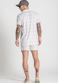 Witte blouse met korte mouwen en bijpassende shorts met een geometrisch patroon. Het shirt heeft een kraag en de outfit wordt aangevuld met lichte schoenen.
