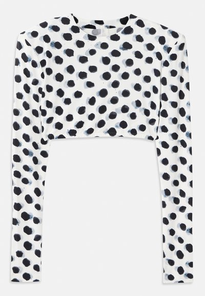 Κομμένο τοπ με μακριά μανίκια από ελαστικό λευκό ύφασμα που έχει σχέδιο με μαύρες βούλες, με απαλό άγγιγμα και στρογγυλή λαιμόκοψη.