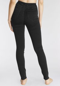 Crne uske traperice od denima s rastezljivim remenom, dva stražnja džepa i vidljivim šavovima uz rubove. Uski kroj do gležnjeva.