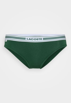 Zeleni bikini spodnji del s klasičnim krojem. Ima bel pas z zelenimi črtami in logotipom "LACOSTE". Gladka tekstura tkanine.