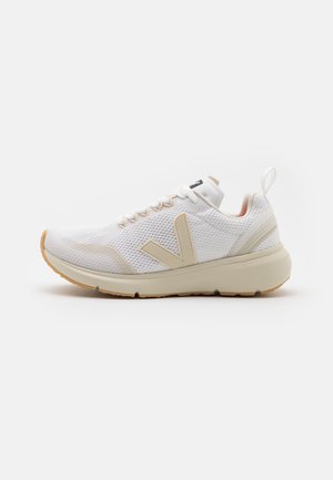 Hvid mesh atletiksko med beige accenter, tyk sål, snørelukning foran og trækflig på hælen, vist fra siden mod en hvid baggrund.