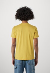Yellow cotton t-shirt with a round neck, short sleeves, and a smooth texture, viewed from the back. Worn with light blue denim cargo pants.