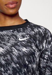 Schwarz Sportoberteil mit abstraktem grauem Muster, Rundhalsausschnitt und kurzen Ärmeln. Mit einem weißen Nike-Logo auf der oberen linken Seite. Glatte Textur.