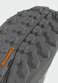 Grå sula på sneakers med aggressivt mönster, som har upphöjda gummidubbar och ett centralt spår. Märkbar orange "Continental"-logotyp.