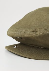 Olive green cap with a flat peak, made of textured fabric. Features include a silver snap button and stitched detailing.