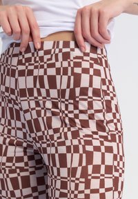 Bruine en crèmekleurige legging met een geruite patroon, met een gladde textuur en een lichte rekking, gedragen op de taille.