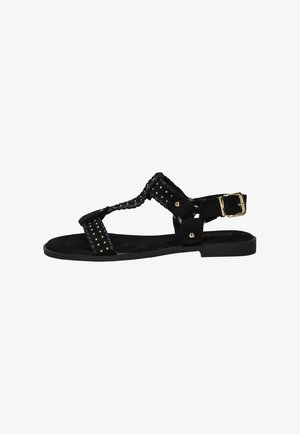 Zwarte platte sandaal met gouden studs, gevlochten bandjes en een gouden gesp aan de enkel.