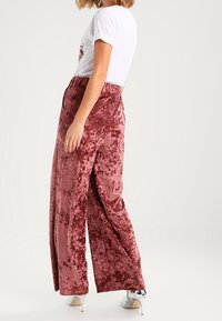 Samtige weite Hosen in staubigem Rosé, mit hoher Taille und seitlichen Schlitzen, kombiniert mit einem enganliegenden weißen T-Shirt und silbernen Absätzen.
