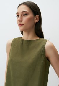 Top senza maniche verde oliva realizzato in tessuto testurizzato. Presenta un colletto a barca e una vestibilità comoda, con dettagli di cucitura visibili.