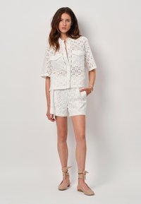 Witte broderie anglaise blouse met korte mouwen en twee borstzakken, gecombineerd met bijpassende korte broek. Gedetailleerd met uitsparingen over het geheel.