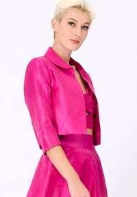 Veste cropped en satin fuchsia avec col rond et manches trois-quarts, présentant une texture lisse et brillante ainsi qu'un design minimaliste.