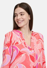 Bunte Bluse mit einer Mischung aus rosa und roten Blumenmustern, aus weichem Stoff gefertigt, mit einem V-Ausschnitt und dezenten Nähdetails.