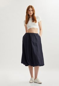 Gonna a palloncino blu navy con vita elasticizzata, dotata di tasche laterali. Abbina con una camicia corta bianca e sneakers di colore chiaro.