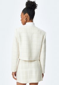Giacca bianca in tweed tagliata con motivo testurizzato e mini gonna coordinata, caratterizzata da un design a quadri e maniche lunghe con dettagli ai polsini.