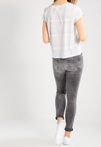 Hvid kortærmet top med et tekstureret mønster, parret med tætsiddende bleget grå jeans og hvide sneakers.