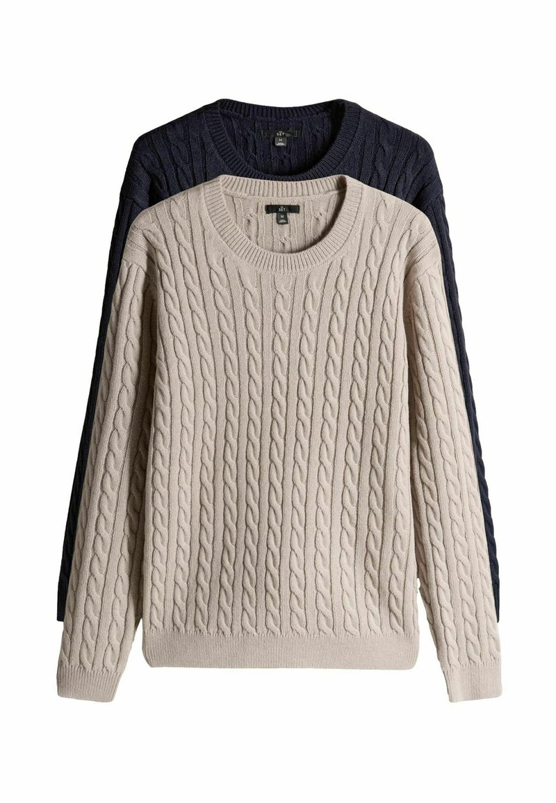 Dva džempera od pletene vune, jedan bež i jedan tamnoplavi, s okruglim izrezima i rebrastim manžetama, prikazani slojevito s teksturiranim uzorcima.