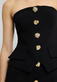Černý bezramenný top se strukturovaným designem, zdobený zlatými ozdobnými knoflíky a dvěma předními kapsami s texturovaným povrchem.