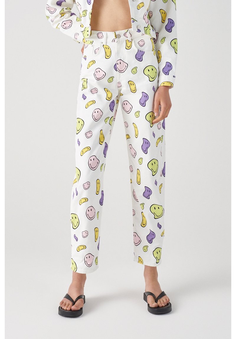 Pantalones blancos con un patrón divertido de caras sonrientes de colores y formas abstractas en amarillo, verde, púrpura y rosa. Corte de pierna recta.