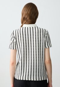Polo à manches courtes en tricot texturé blanc avec des rayures verticales noires et un col classique.