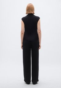 Top preto justo com mangas curtas, combinado com calças pretas de perna larga. Textura suave, design minimalista, visto pelas costas.