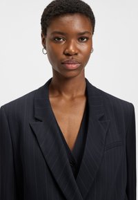 Navy pinstriped blazer with a notch lapel, single button closure, and a chest pocket. Fabric appears smooth with a tailored fit.