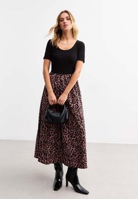 Black ribbed short-sleeve top paired with a long, pink leopard-print skirt. The outfit includes black heeled boots and a textured black handbag.
