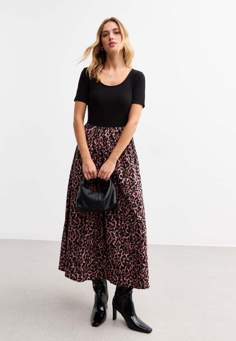Black ribbed short-sleeve top paired with a long, pink leopard-print skirt. The outfit includes black heeled boots and a textured black handbag.