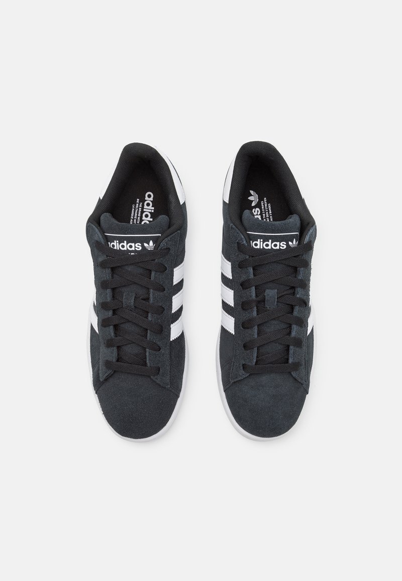 Zapatillas de ante negro con rayas blancas, punta redonda, cordones planos, cuello acolchado y superficie texturizada. Logo visible en la lengüeta y en las plantillas.