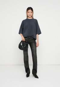Mørk grå oversized genser med brede ermer, sammen med svarte straight-leg jeans. Holder en svart skinnveske. Ren bakgrunn.