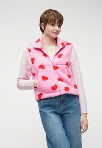 Φλις ζακέτα με φερμουάρ σε ροζ χρώμα με κόκκινες καρδιές; διαθέτει μακριά, ανοιχτό ροζ μανίκια και τσέπη μπροστά.