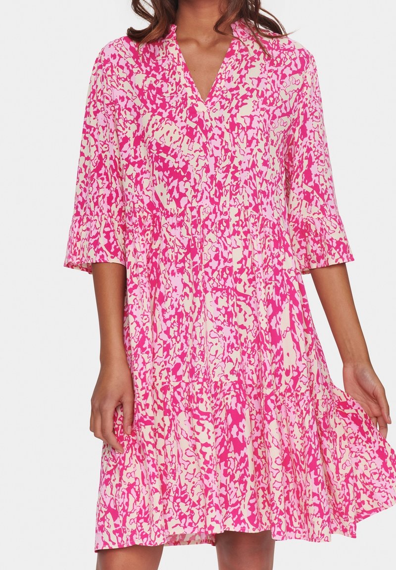 Kortärmad klänning i rosa och kräm med en splattertryck, med V-hals och en tiered kjoldesign. Lättviktigt tyg med en flytande passform.