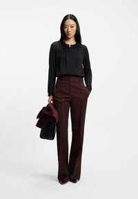 Blusa nera con pieghe, abbinata a pantaloni bordeaux a vita alta con tasche laterali. Accessoriata con una borsa nera e un giubbotto bordeaux.