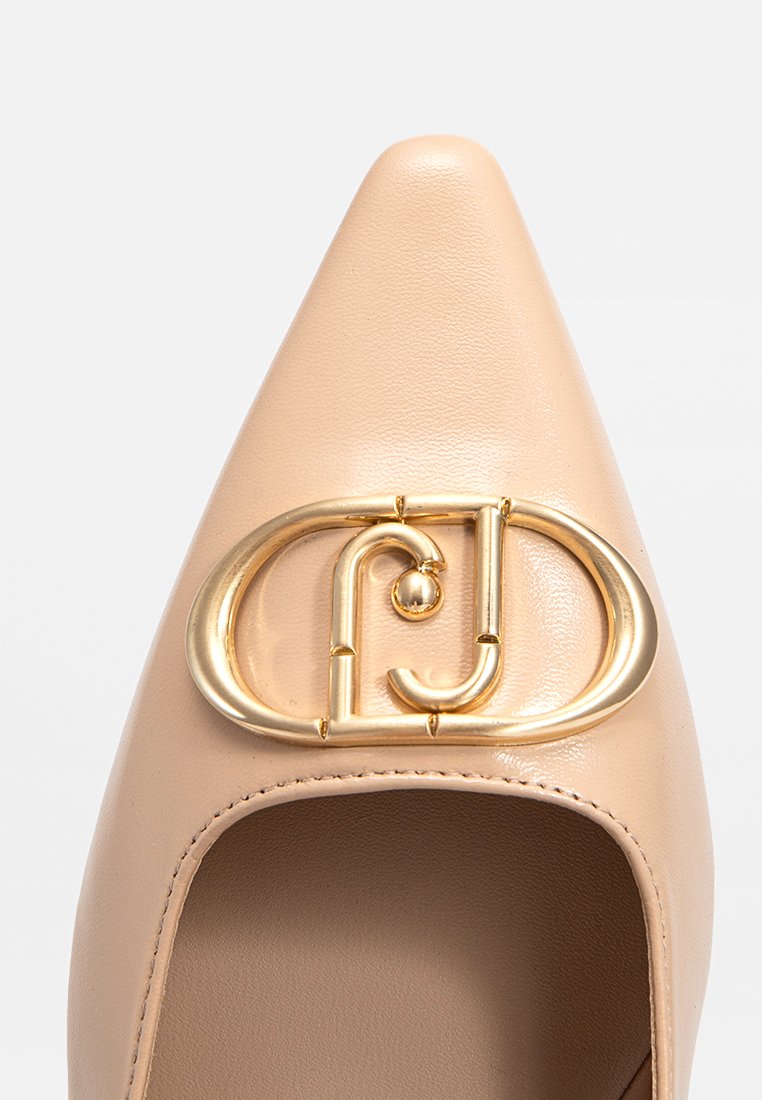 Pump in pelle beige con punta affusolata e lato aperto. Presenta una grande fibbia decorativa in oro sulla tomaia, che mette in evidenza una texture morbida.