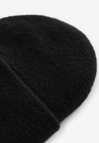 Musthave mustrikott, millel on tekstuuriga viimistlus, ümardatud ülaosa ja volditud ääre, mis tagab lisasoojus ja mugavus.